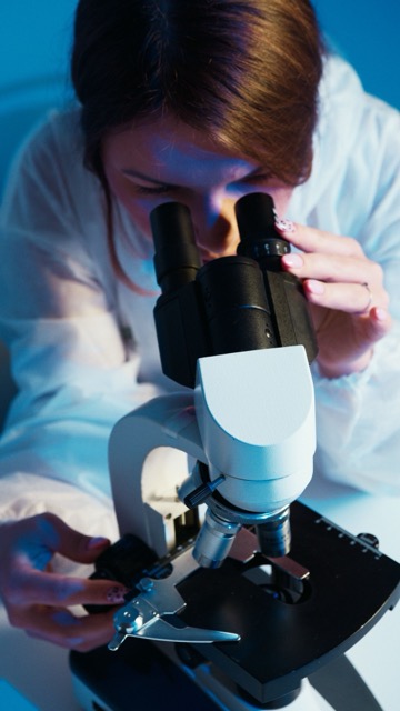 Scientist in a lab coat using a microscope, focusing on a slide under blue lighting.