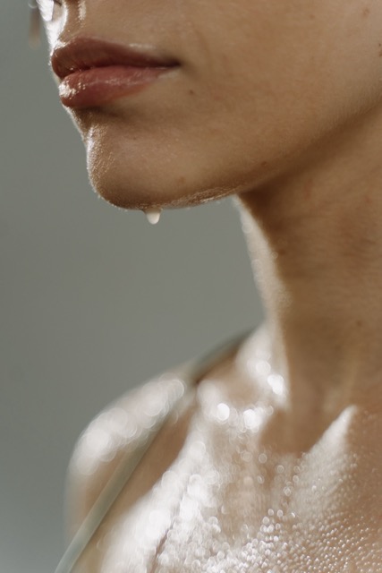 Close-up of a person’s lower face and neck with a drop of water hanging from the chin and beads on the skin.